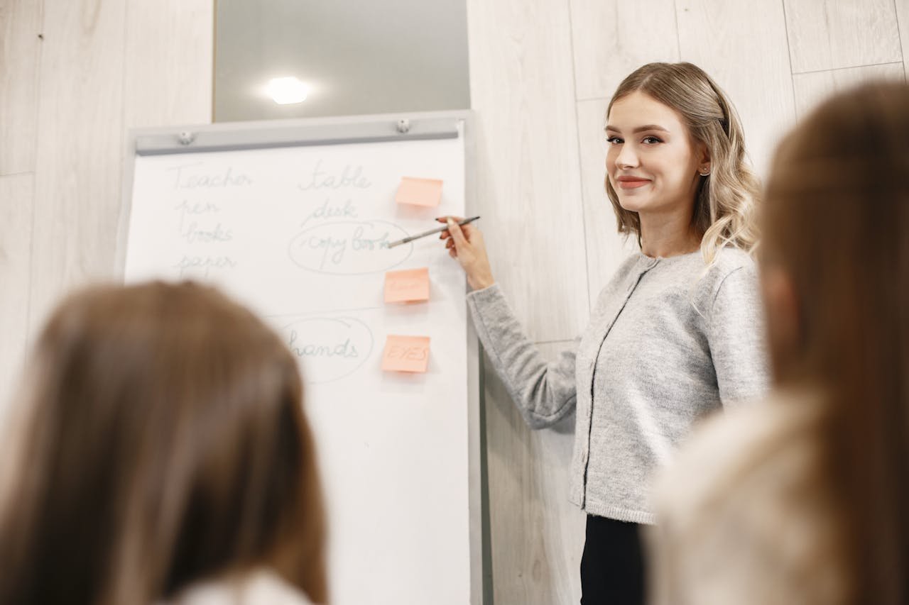 Female teacher smiling as she explains notes on a flipchart to a class.